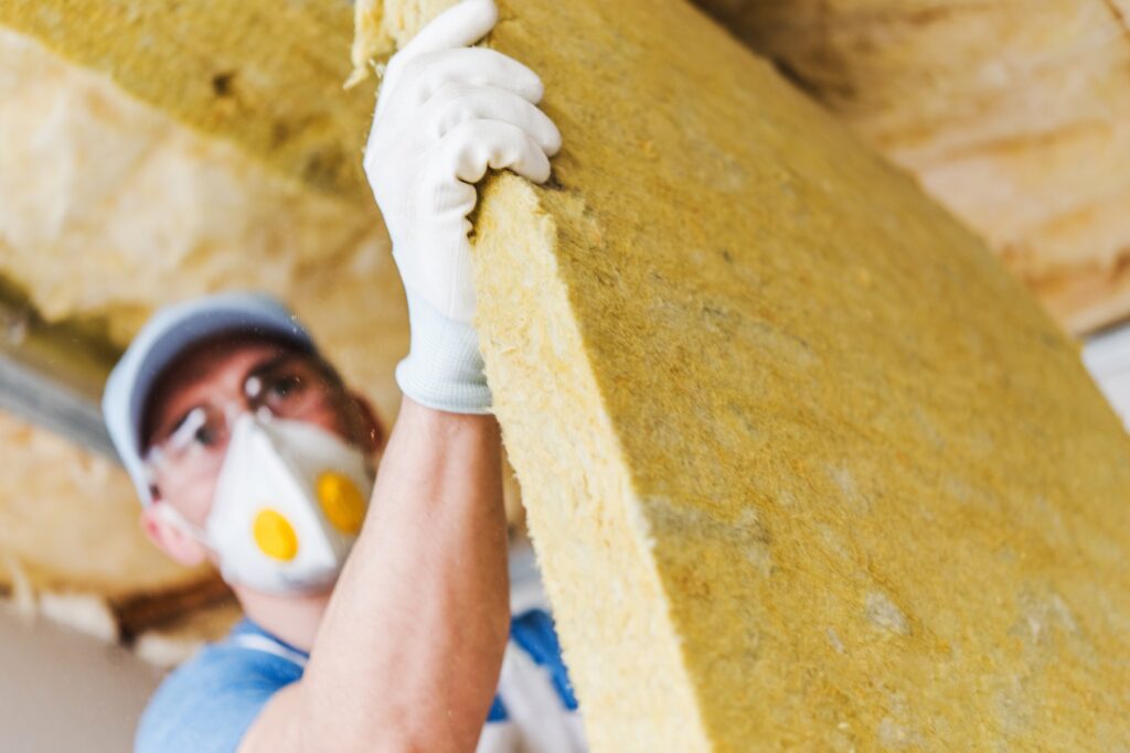 Bauarbeiter mit einem Stück Dämmmaterial, Dachdämmung mit Mineralwolle.