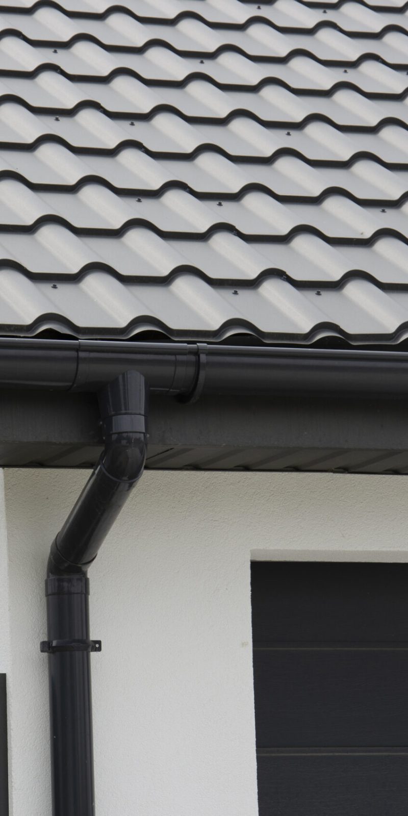 Schwarzes Kunststoff-Dachrinnensystem und Metallziegel auf dem Dach