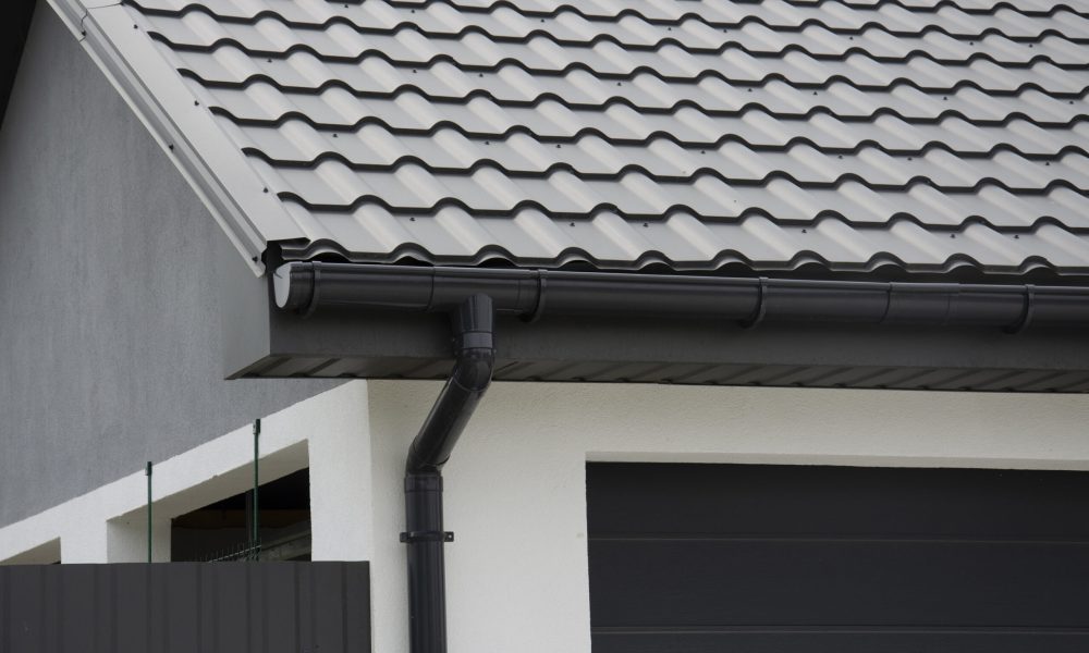 Schwarzes Kunststoff-Dachrinnensystem und Metallziegel auf dem Dach