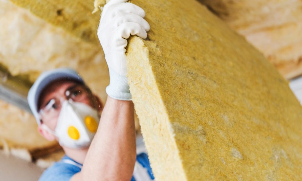 Bauarbeiter mit einem Stück Dämmmaterial, Dachdämmung mit Mineralwolle.